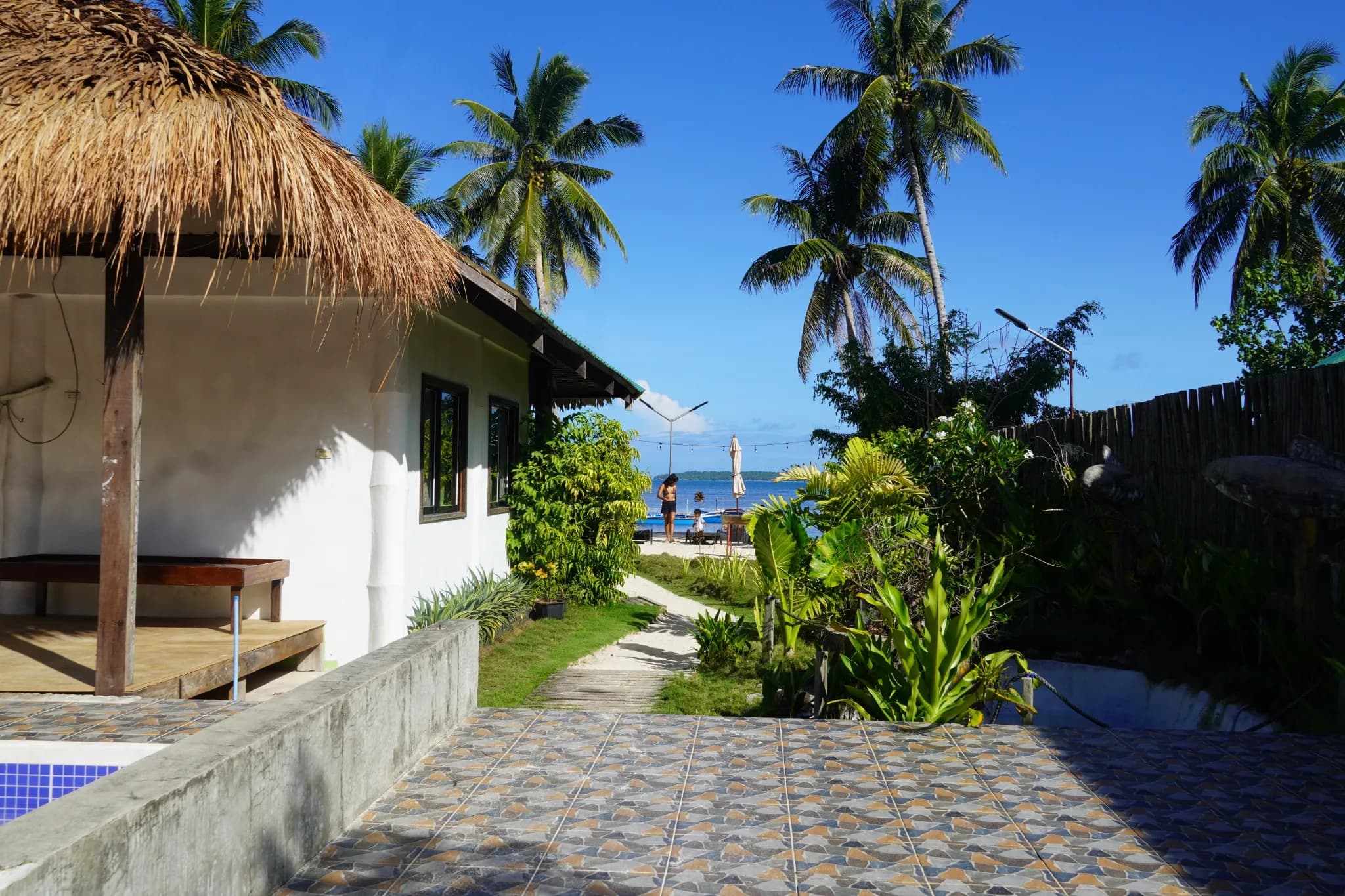 Garden path between a thatched-roof building and tropical plants leading toward the sea at Aggehanan.