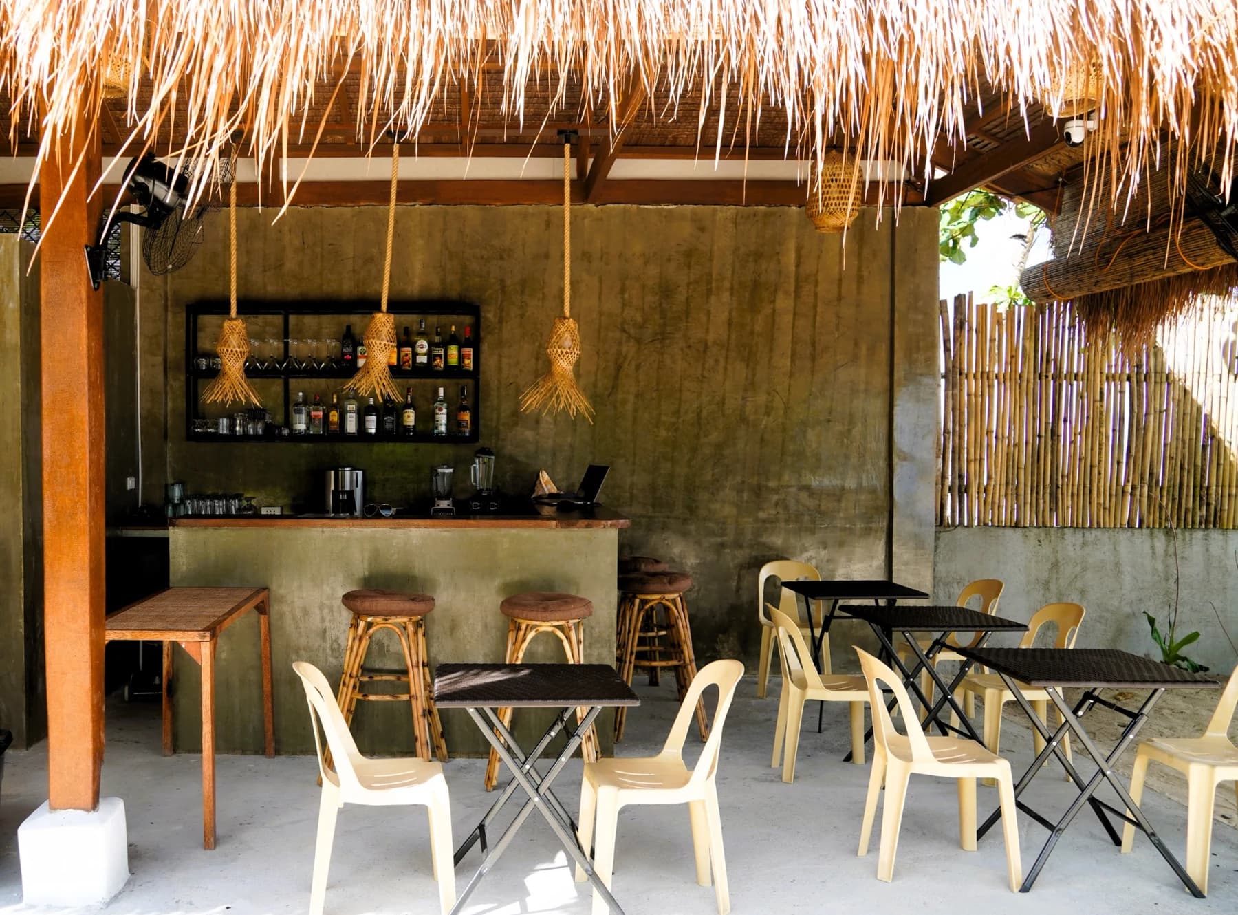 Open-air bar and dining area with a thatched roof, woven pendant lights, bar stools, tables and chairs.