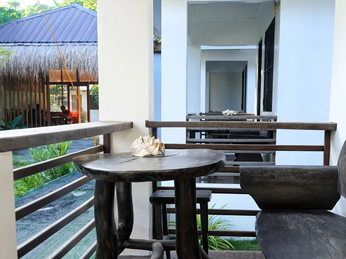 Covered terrace with a round wooden table, a shell decoration, wooden seating and railings.