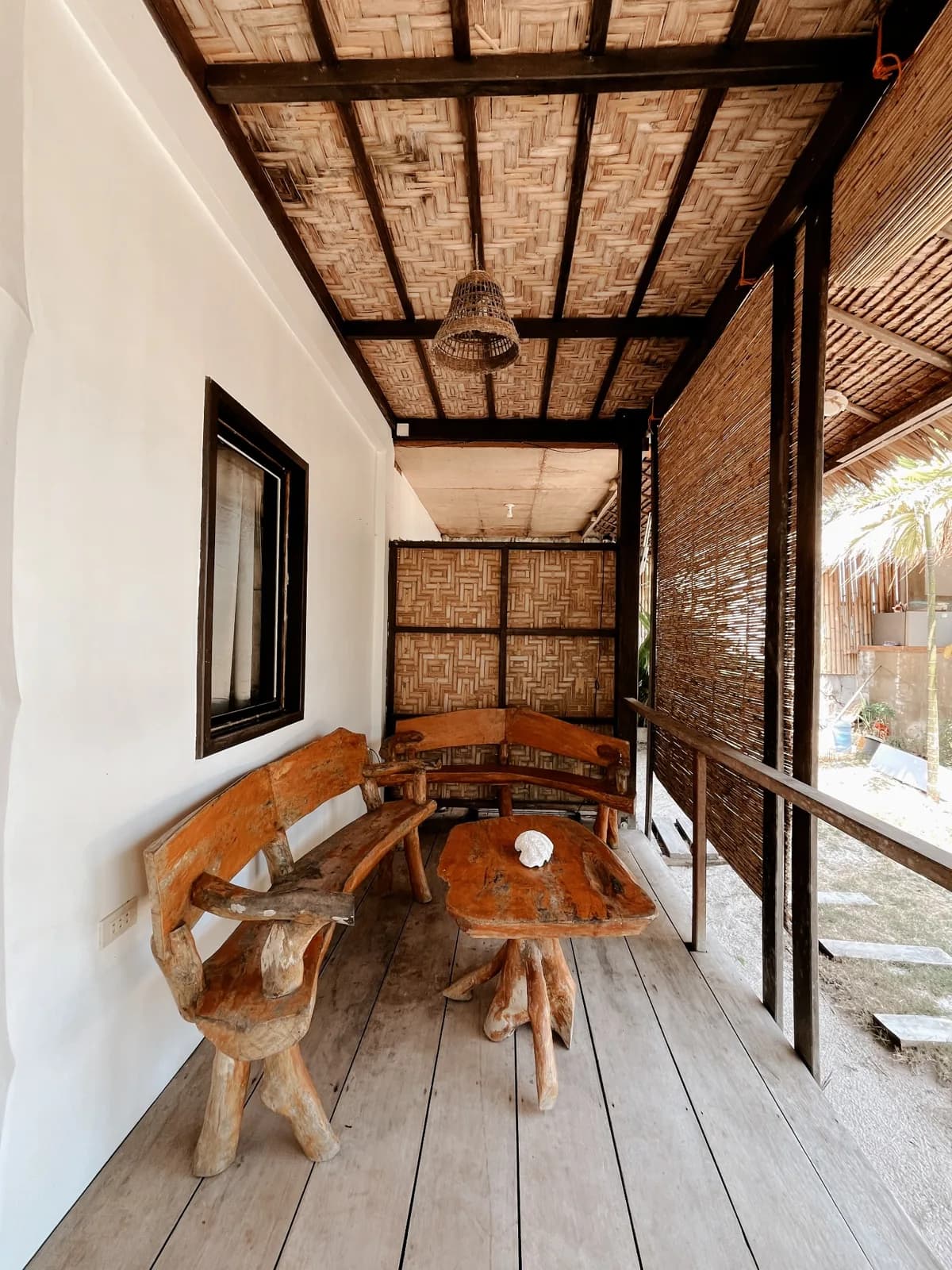 Covered wooden terrace of the Beachfront Bungalow with rustic seating.