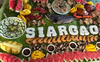 Filipino boodle fight lunch with seafood, grilled fish, meat, rice and tropical fruit during a Siargao island-hopping tour.